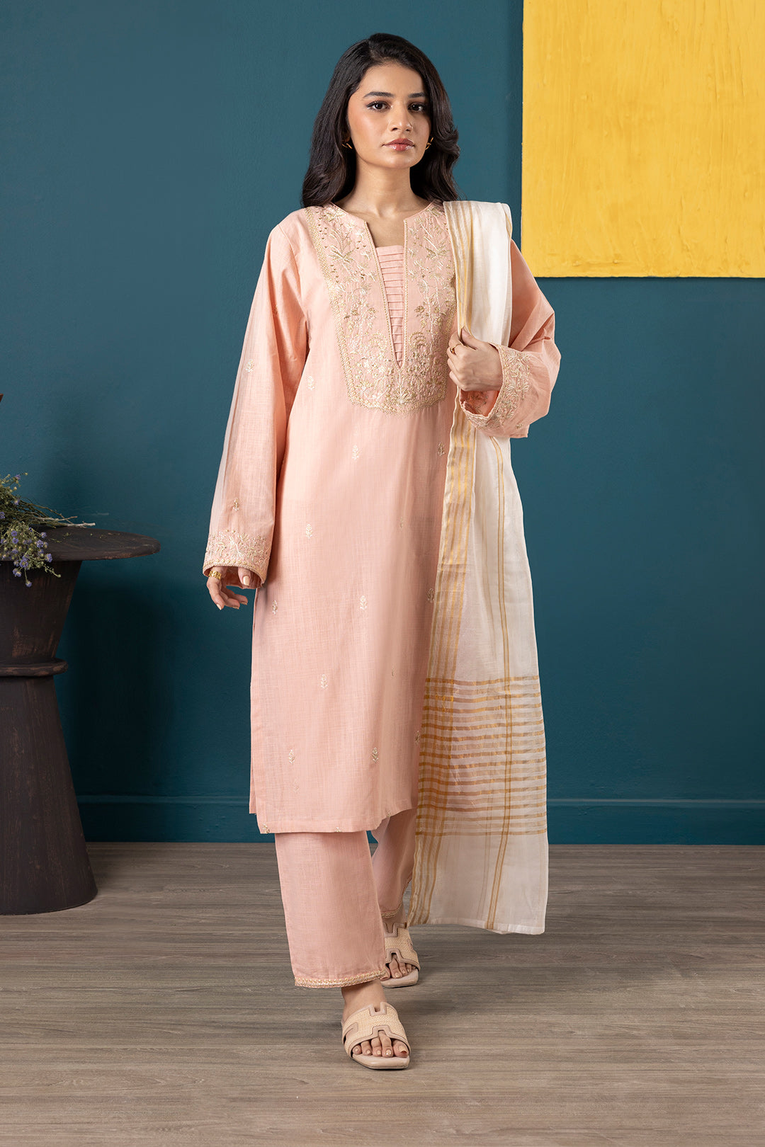 Woman in a pink traditional outfit with a white dupatta against a blue and yellow wall.