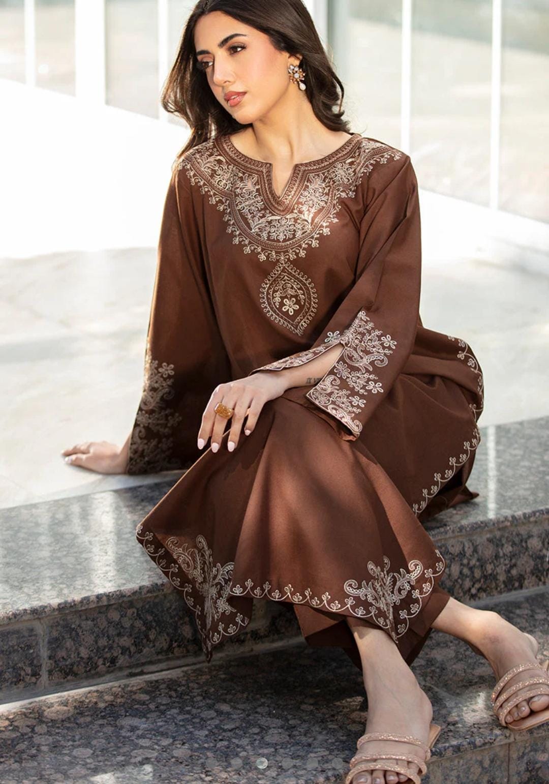 Woman wearing a brown embroidered dress sitting on steps.