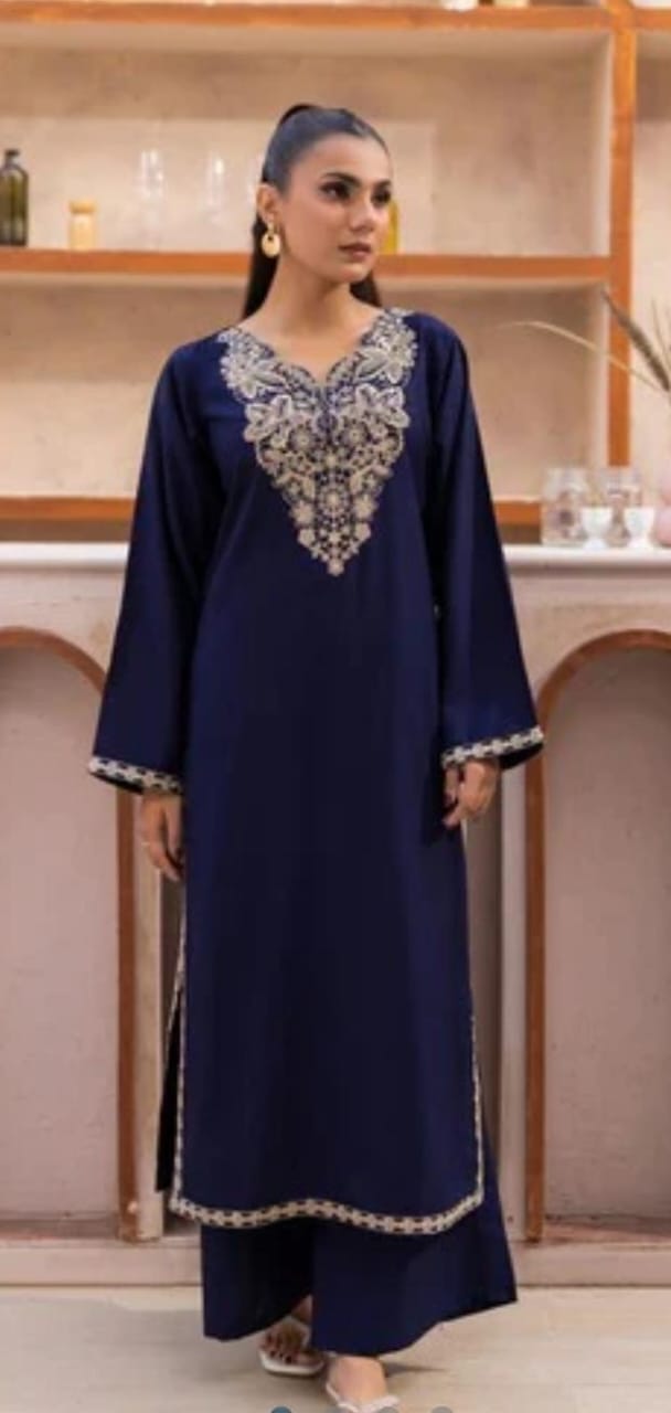 Woman wearing a navy blue dress with intricate white embroidery in a room setting.