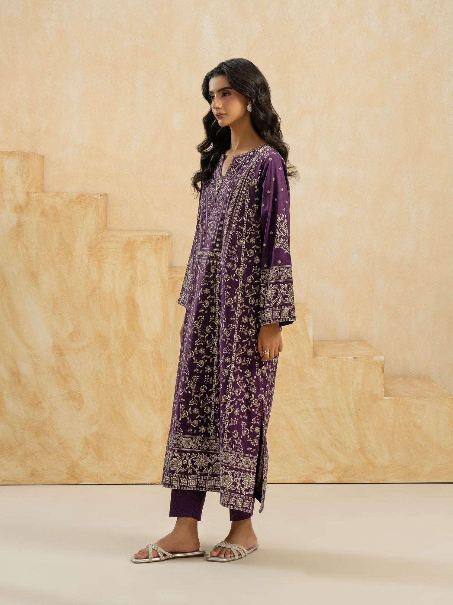 Woman wearing a purple embroidered outfit against a beige background