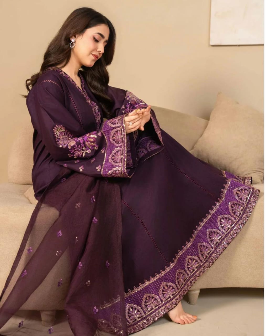 Woman in a purple traditional outfit sitting on a beige couch.