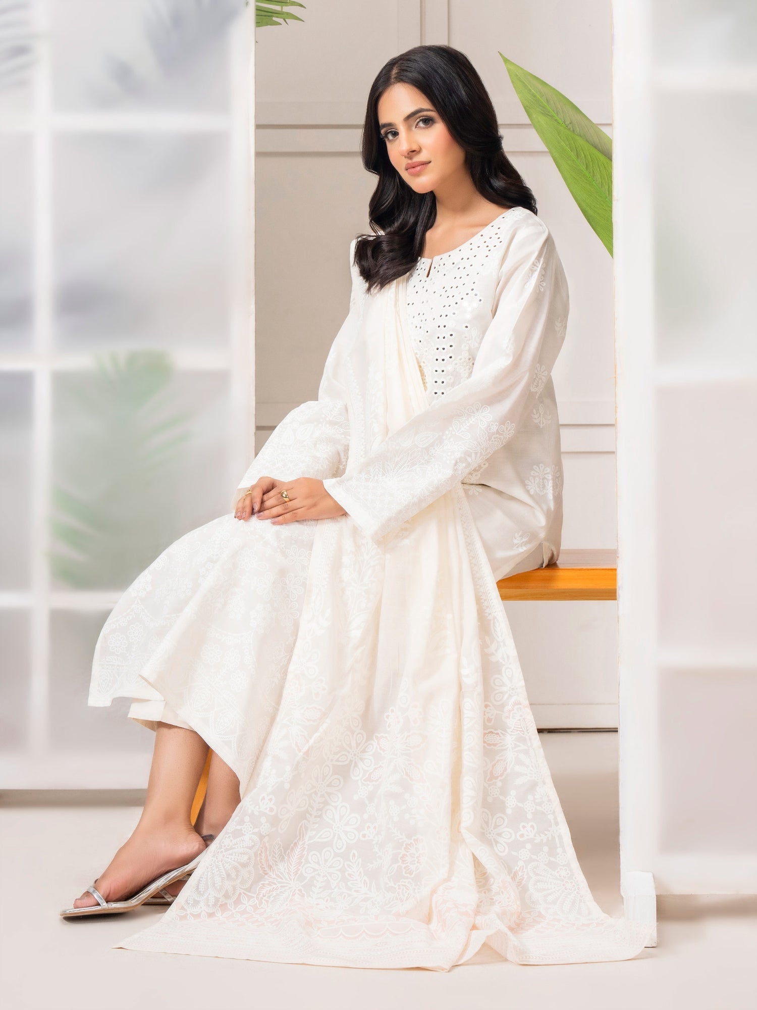 Woman in a white dress sitting on a bench with a light background