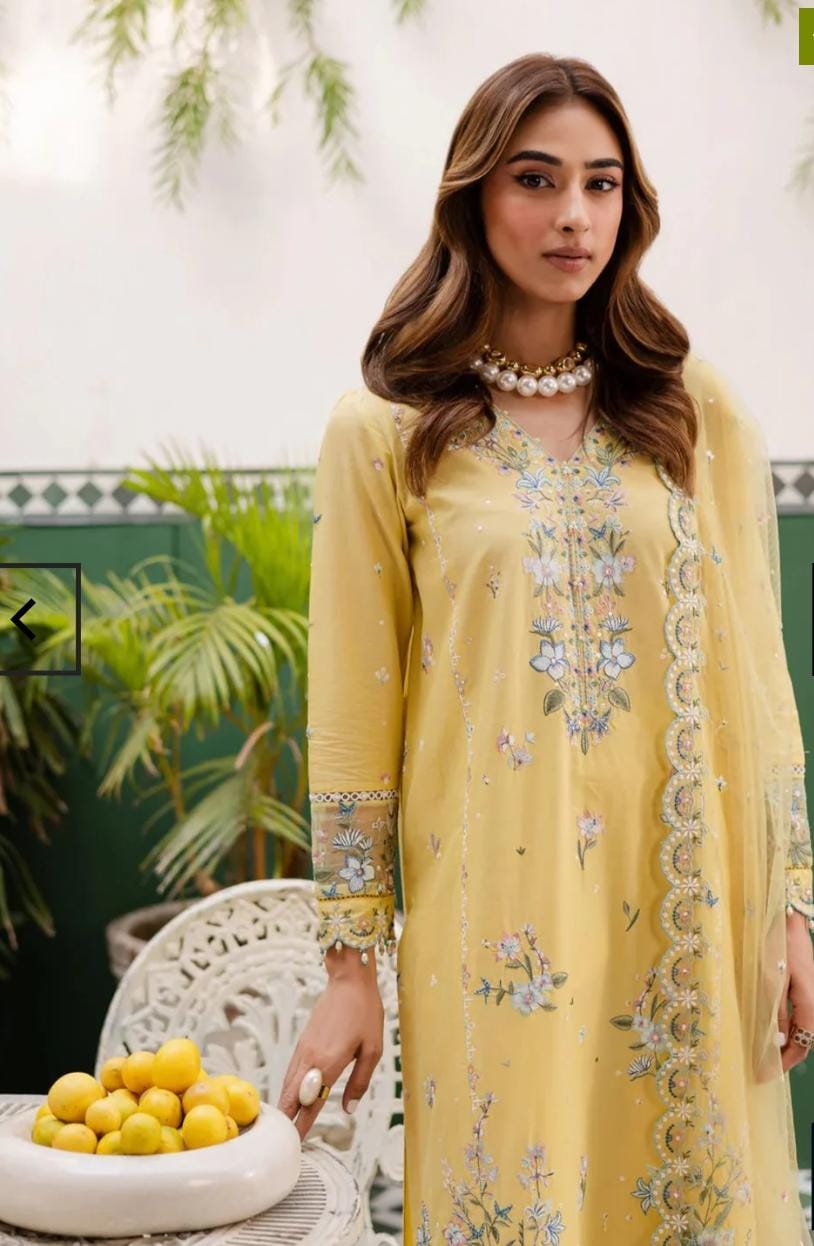 Woman wearing a yellow embroidered dress sitting outdoors with plants in the background